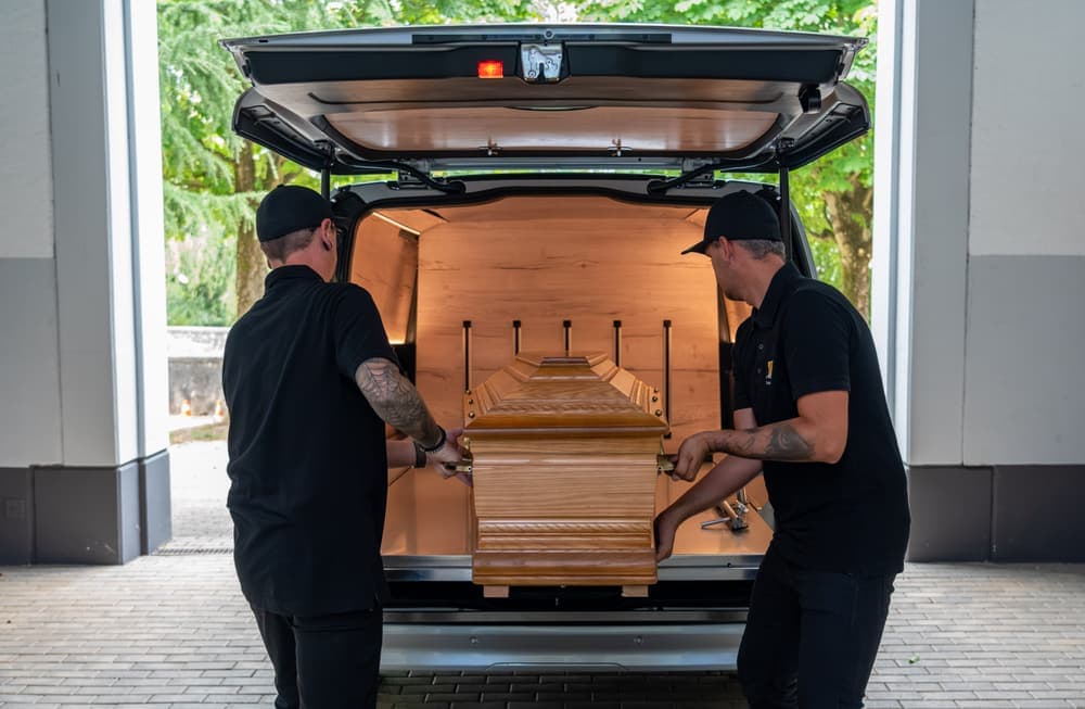Ein Sarg wird in den Bestattungswagen geladen